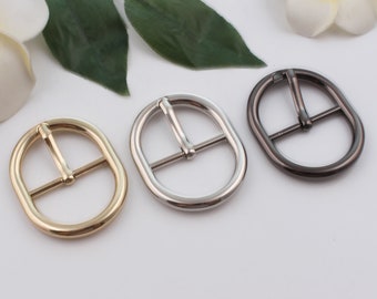 May include: Three oval-shaped metal belt buckles in gold, silver, and black.