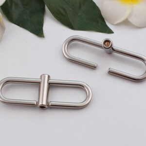 May include: Two silver metal clasps, one with a small gold pin, for attaching to a bag or other item.