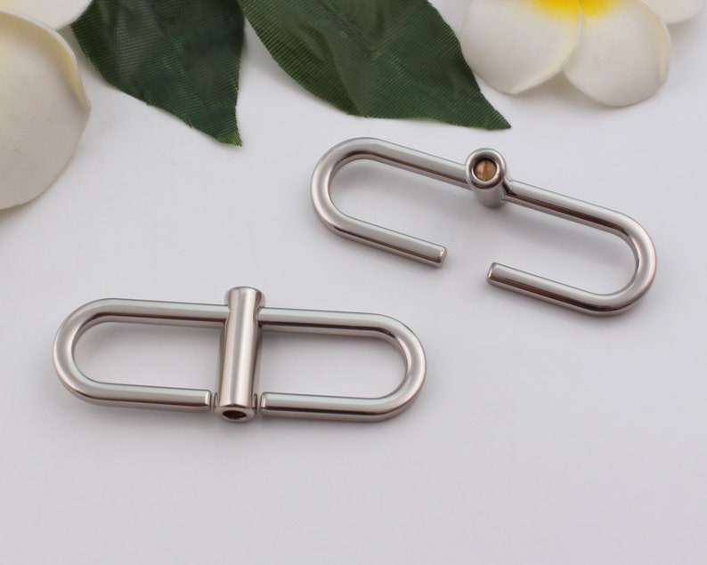 May include: Two silver metal clasps, one with a small gold pin, for attaching to a bag or other item.