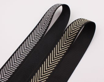 May include: Two black ribbons with chevron patterns. One ribbon has a white chevron design, and the other has a beige chevron design. The ribbons are made of a sturdy material and are suitable for various crafting projects.