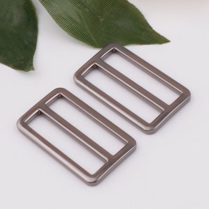 May include: Two silver metal slider buckles. The buckles are rectangular with a rounded edge and have a single slot in the center.
