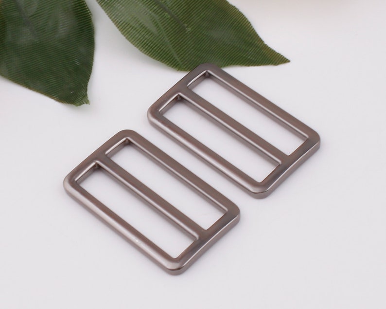 May include: Two silver metal slider buckles. The buckles are rectangular with a rounded edge and have a single slot in the center.