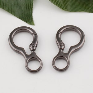 May include: Two black metal swivel clasps with a loop on each side. The clasps are designed for attaching to bags, straps, or other items.