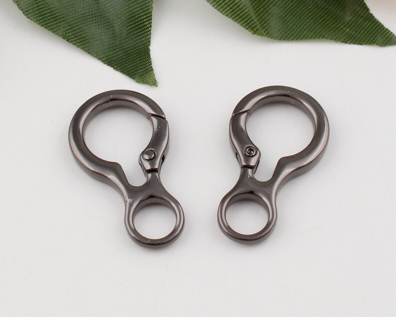 May include: Two black metal swivel clasps with a loop on each side. The clasps are designed for attaching to bags, straps, or other items.