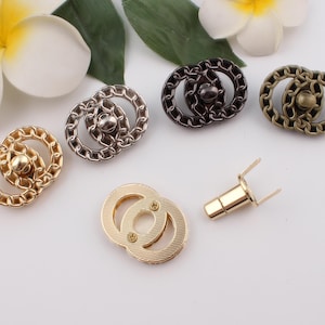 Puede incluir: Cinco cierres de metal de color dorado con un diseño de eslabón de cadena. Los cierres son de varios tamaños y están dispuestos sobre una superficie blanca.