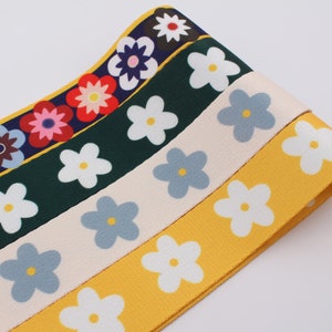 Op de afbeelding: Vier rollen stoffen lint met een madeliefjesprint. De linten zijn geel, cr&egrave;me, blauw en groen met witte madeliefjes.