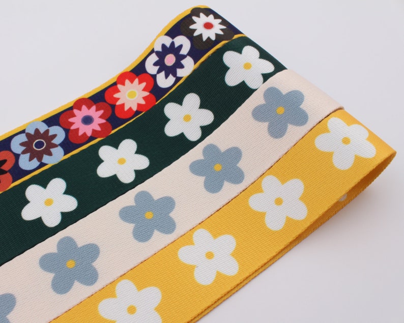 Op de afbeelding: Vier rollen stoffen lint met een madeliefjesprint. De linten zijn geel, cr&egrave;me, blauw en groen met witte madeliefjes.