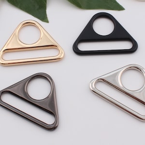 Op de afbeelding: Vier driehoekige metalen schuifgespen in goud, zwart, zilver en gunmetal.