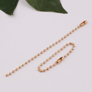 May include: A gold-colored ball chain with two clasps. The chain is made of small, round beads.