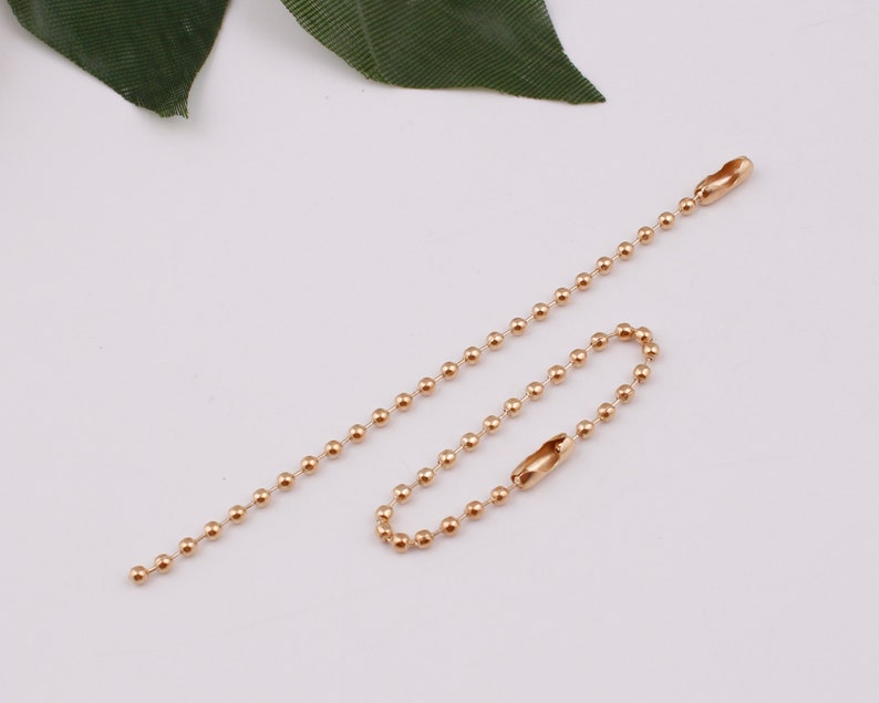 May include: A gold-colored ball chain with two clasps. The chain is made of small, round beads.