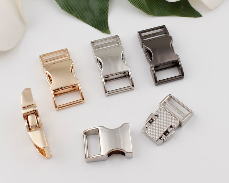 Op de afbeelding: Vijf metalen gespen in verschillende afwerkingen: goud, zilver, nikkel en zwart. De gespen zijn allemaal even groot en hebben dezelfde vorm, met een rechthoekig lichaam en een gebogen gesp.