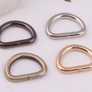 Puede incluir: Cuatro anillos metálicos en forma de D en diferentes acabados: plata, negro, oro y latón antiguo. Los anillos tienen un diámetro de aproximadamente 2,5 cm.