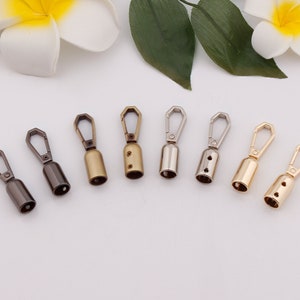 Peut inclure: Huit crochets pivotants en métal dans différentes finitions, notamment argent, or et bronze. Les crochets sont tous de la même taille et de la même forme, et ils ont une petite boucle en haut pour être attachés à une sangle ou une chaîne.