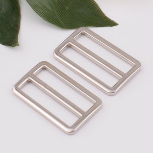 May include: Two silver metal slider buckles. The buckles are rectangular with a single, centered, horizontal bar.