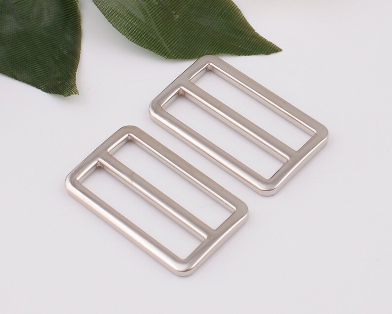 May include: Two silver metal slider buckles. The buckles are rectangular with a single, centered, horizontal bar.