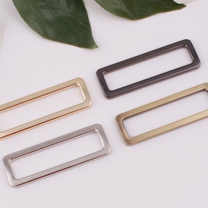 May include: Four metal rectangular rings in different finishes: gold, silver, brass, and black. These rings are ideal for attaching to straps, bags, or other accessories.