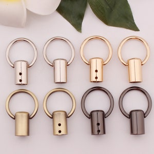 Può includere: Sette portachiavi in metallo con un anello rotondo e un perno cilindrico. I portachiavi sono in argento, oro e nero.