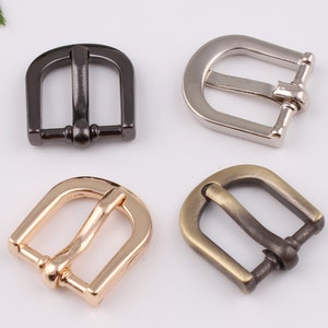 Puede incluir: Cuatro hebillas de cinturón metálicas en diferentes acabados: negro, plateado, dorado y latón antiguo. Cada hebilla tiene una forma rectangular simple con la parte superior redondeada y una sola lengüeta.