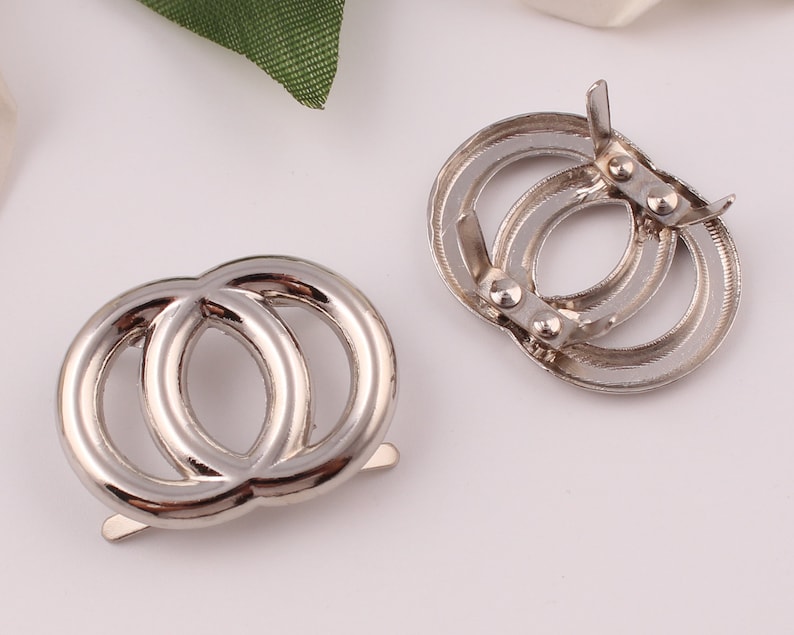 Pu&ograve; includere: Due anelli in metallo argentato con un design a doppio anello. Gli anelli sono collegati da una chiusura in metallo.