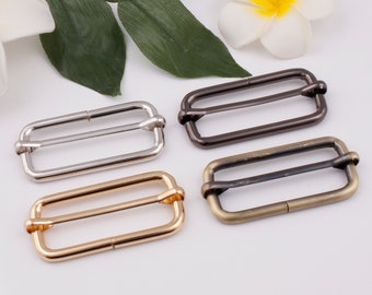 May include: Four metal slider buckles in different finishes: silver, gold, antique brass, and black. Each buckle has a rectangular shape with two parallel bars.