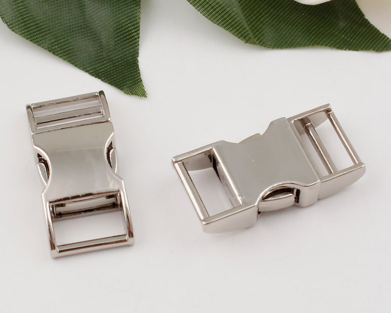 Op de afbeelding: Twee zilveren metalen zij-ontgrendelingsgespen. De gespen zijn ontworpen voor gebruik met band of riemen.