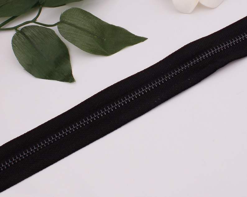 May include: A black zipper with a metal slider. The zipper is closed and the teeth are visible.