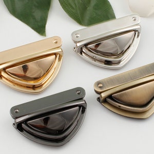 Puede incluir: Cuatro cierres metálicos en diferentes acabados: dorado, plateado, negro y latón antiguo. Cada cierre tiene una pieza superior rectangular y una pieza inferior triangular.