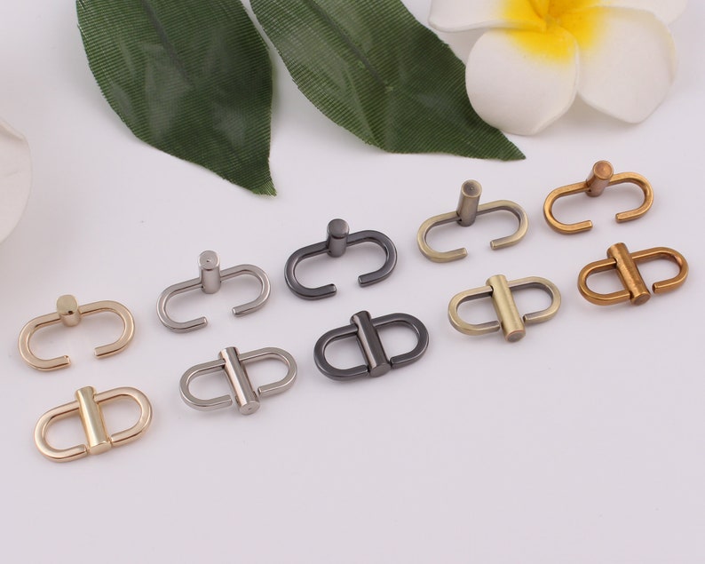 Op de afbeelding: Assortiment van acht metalen D-ringgespen in verschillende afwerkingen, waaronder zilver, goud en antiek messing. De gespen zijn allemaal even groot en hebben dezelfde vorm, met een gladde, gepolijste afwerking.