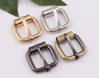 May include: Four metal belt buckles in different finishes: gold, silver, black, and antique brass. Each buckle is square shaped with a smooth, polished finish.