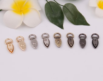 May include: Assortment of ten metal D-ring hardware in various finishes, including gold, silver, and bronze. The D-rings are in a teardrop shape with a flat back and two small holes.
