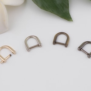 May include: Four metal D-rings in different finishes: gold, silver, antique brass, and black. The rings are approximately 1 inch in diameter.