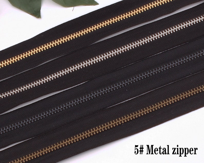 May include: Four black zipper tapes with different colored metal teeth. The teeth are gold, silver, black, and gold. The text "5# Metal zipper" is at the bottom of the image.
