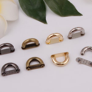 May include: Assortment of metal D-ring hardware in silver, gold, and bronze finishes. The rings are various sizes and styles, some with flat backs and others with screw-on backs.