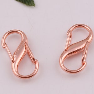 Pu&ograve; includere: Due chiusure a moschettone in metallo dorato rosa, ciascuna con un design a forma di otto.