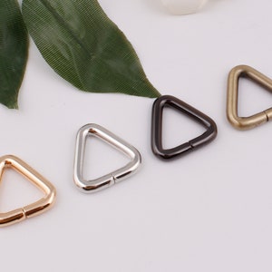 Op de afbeelding: Vier driehoekige metalen ringen in goud, zilver, zwart en brons. De ringen hebben een diameter van ongeveer 2,5 cm.