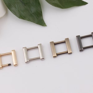 May include: Four metal D-ring hardware pieces in different finishes: gold, silver, antique brass, and black. The rings are approximately 1 inch in diameter.