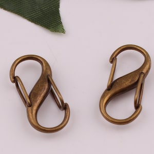 Pu&ograve; includere: Due fermagli o ganci a forma di S in metallo dorato antico. Questi fermagli sono spesso utilizzati per attaccare portachiavi, borse o altri accessori.