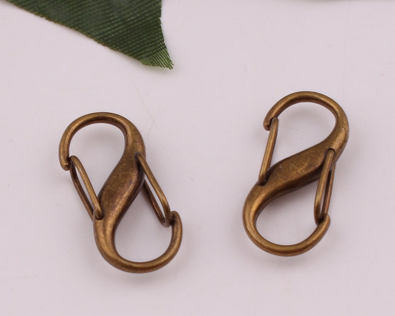 Pu&ograve; includere: Due fermagli o ganci a forma di S in metallo dorato antico. Questi fermagli sono spesso utilizzati per attaccare portachiavi, borse o altri accessori.
