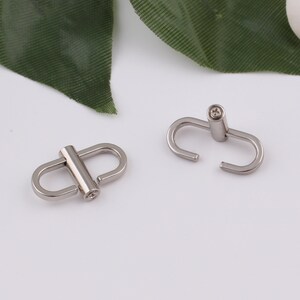 May include: Two silver metal clasps with a round, slightly raised center. The clasps are designed to connect two pieces of material together.