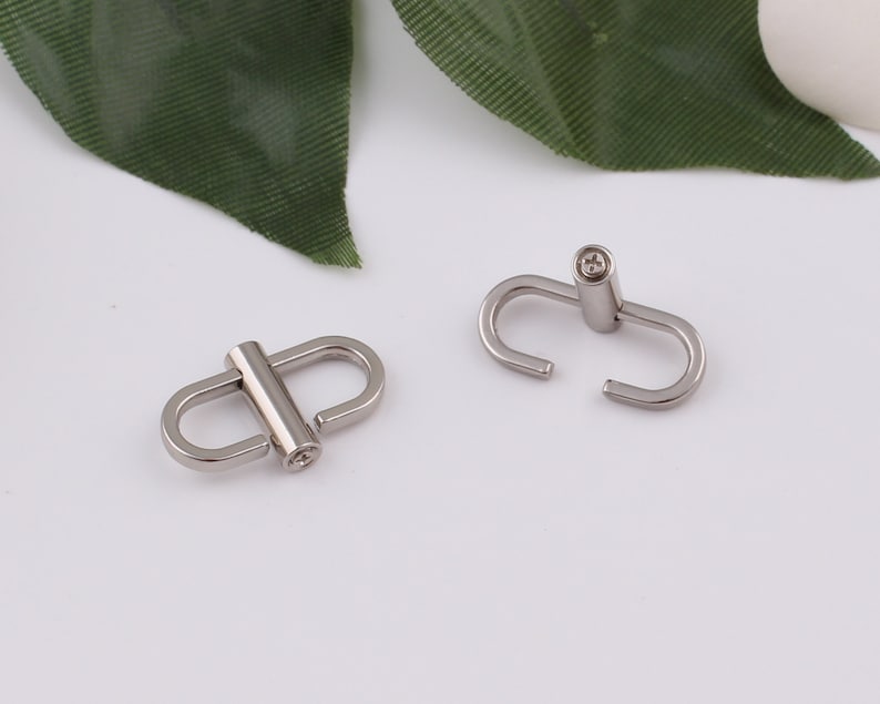May include: Two silver metal clasps with a round, slightly raised center. The clasps are designed to connect two pieces of material together.