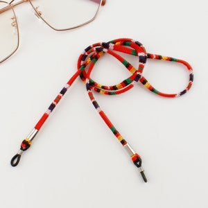 Puede incluir: Cadena de gafas con estampado rojo, negro, blanco y verde con extremos met&aacute;licos plateados.