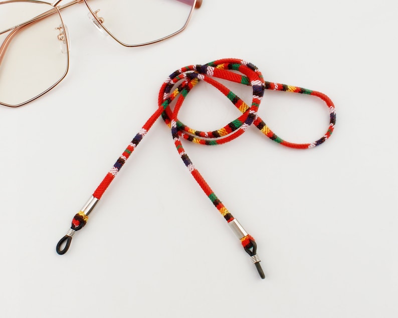Puede incluir: Cadena de gafas con estampado rojo, negro, blanco y verde con extremos met&aacute;licos plateados.