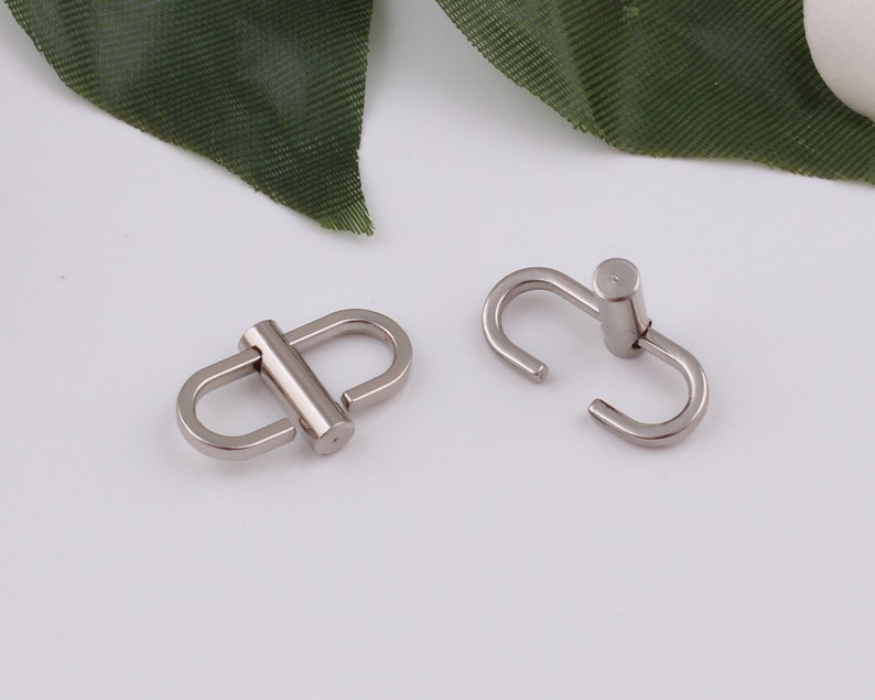 Op de afbeelding: Twee zilveren metalen gespen, een met een rechte stang en de andere met een gebogen stang.