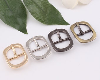 May include: Four metal belt buckles in different finishes: gold, silver, black, and antique brass. Each buckle is oval-shaped with a smooth, rounded edge.