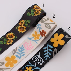 Puede incluir: Tres rollos de cinta de tela negra, blanca y negra con patrones florales. La cinta negra tiene un patrón de girasol, la cinta blanca tiene un patrón floral rosa, azul y marrón, y la cinta negra tiene un patrón de flor amarilla y hojas.