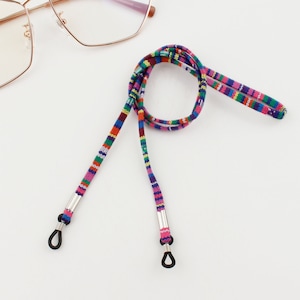 Puede incluir: Una cadena de gafas tejida de colores con extremos de metal plateado y bucles de goma negra. La cadena est&aacute; hecha de una variedad de colores, incluyendo rosa, azul, rojo y verde.