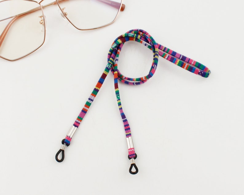 Puede incluir: Una cadena de gafas tejida de colores con extremos de metal plateado y bucles de goma negra. La cadena est&aacute; hecha de una variedad de colores, incluyendo rosa, azul, rojo y verde.