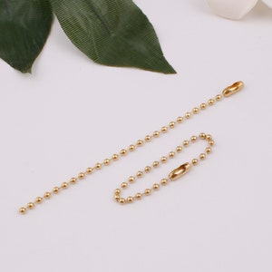 May include: Two gold ball chain keychains with a loop at one end and a clasp at the other end.