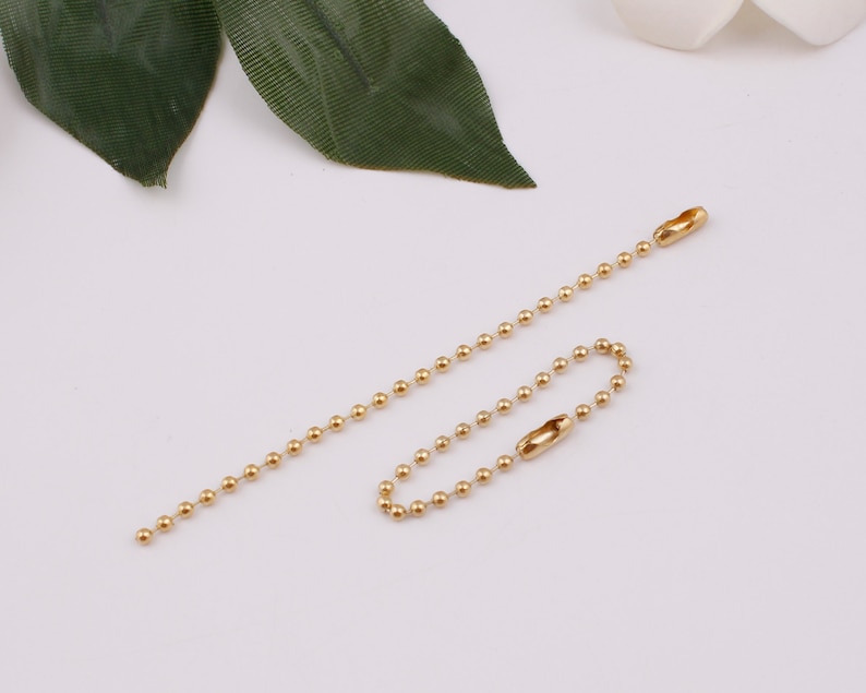 May include: Two gold ball chain keychains with a loop at one end and a clasp at the other end.