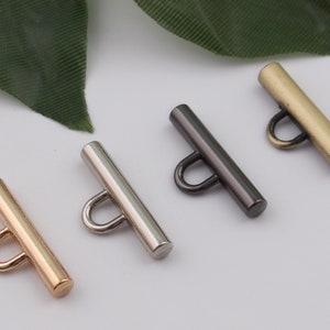 May include: Four metal T-bar toggles in gold, silver, black, and bronze. Each toggle has a loop at the top and a straight bar.